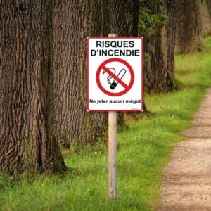 Panneau "Risques d'incendie - Ne jeter aucun mégot" installé sur un poteau le long d'un chemin forestier